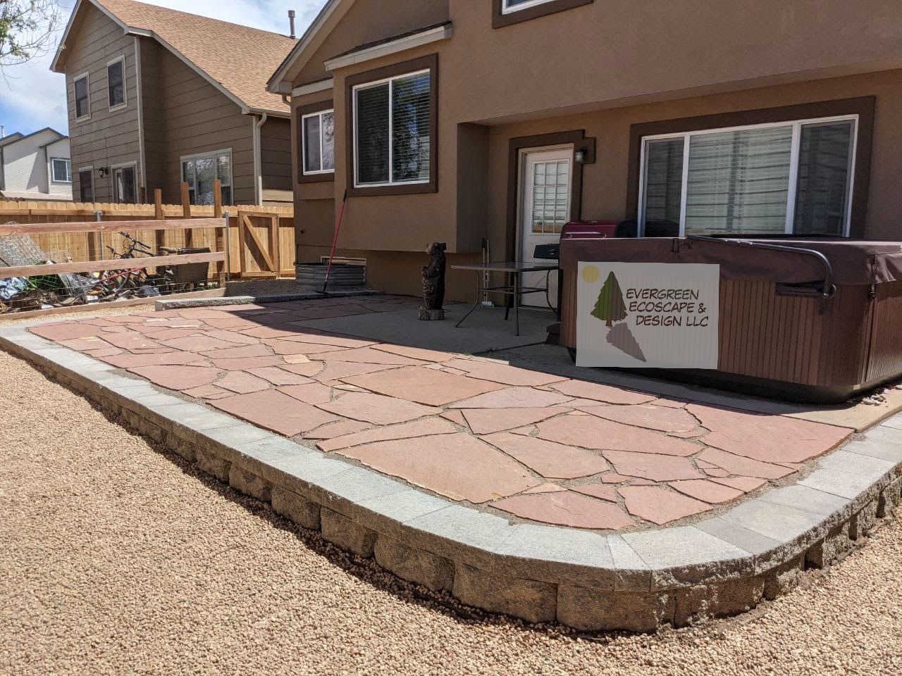 Backyard patio with stamped concrete, hot tub, and wooden deck beside a tan house.