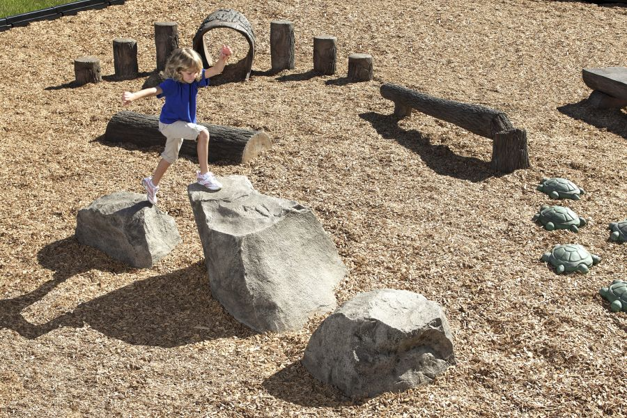 Child jumping between large rocks in a woodchip playground
