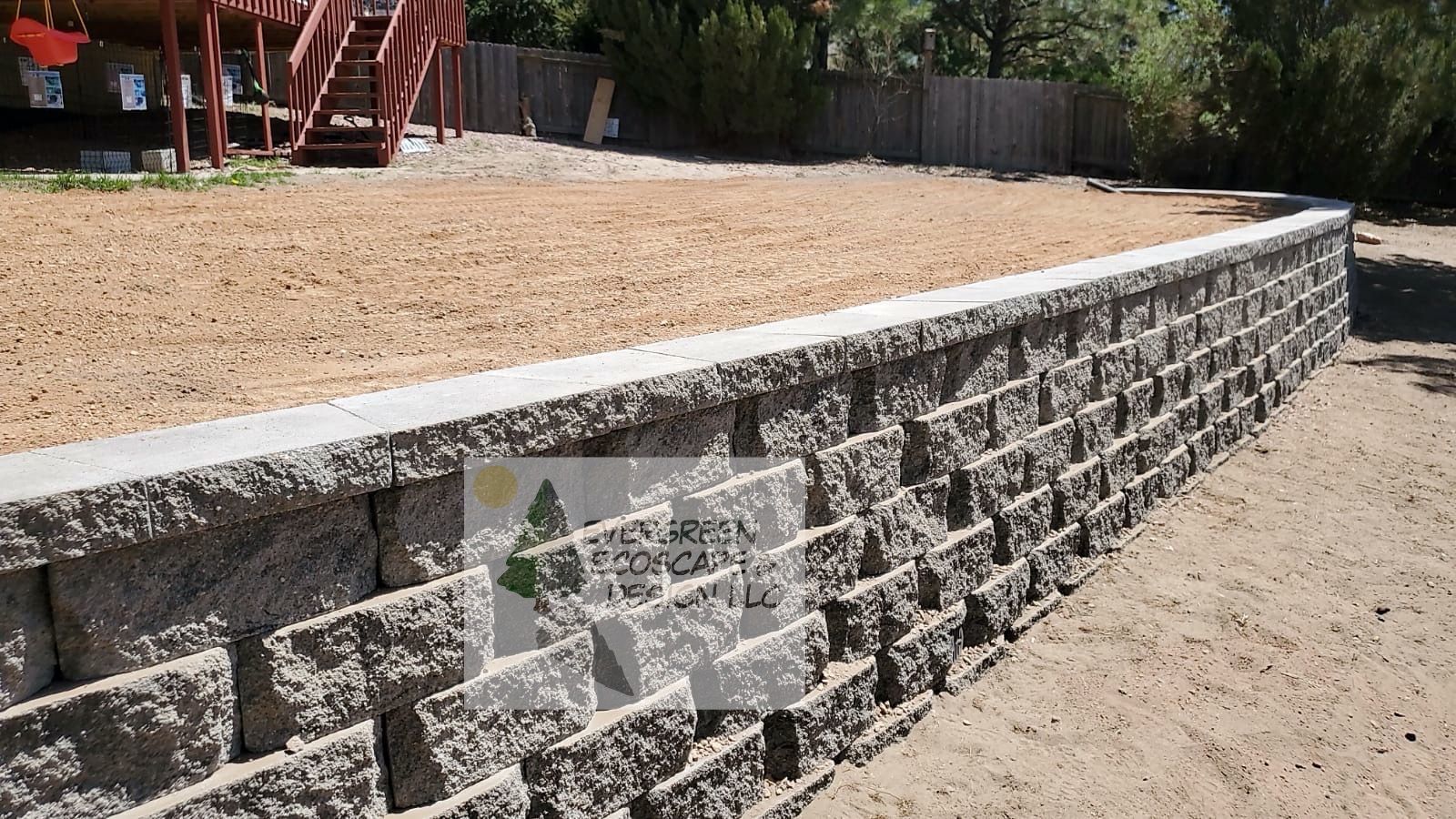 Stone retaining wall edging a raised gravel yard beside a driveway, with red stairs in the background
