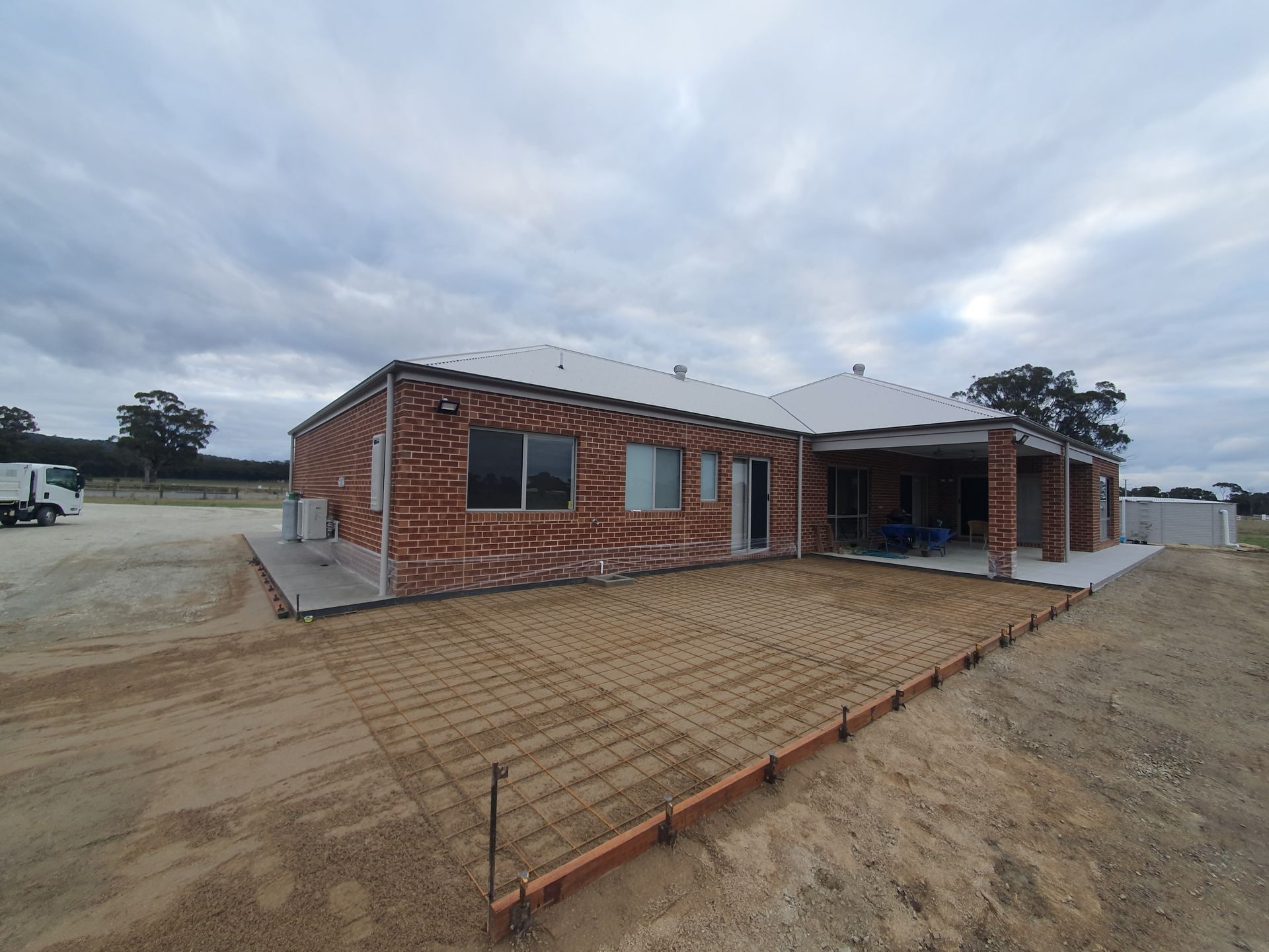 A brick house with a white roof is sitting in the middle of a dirt field.