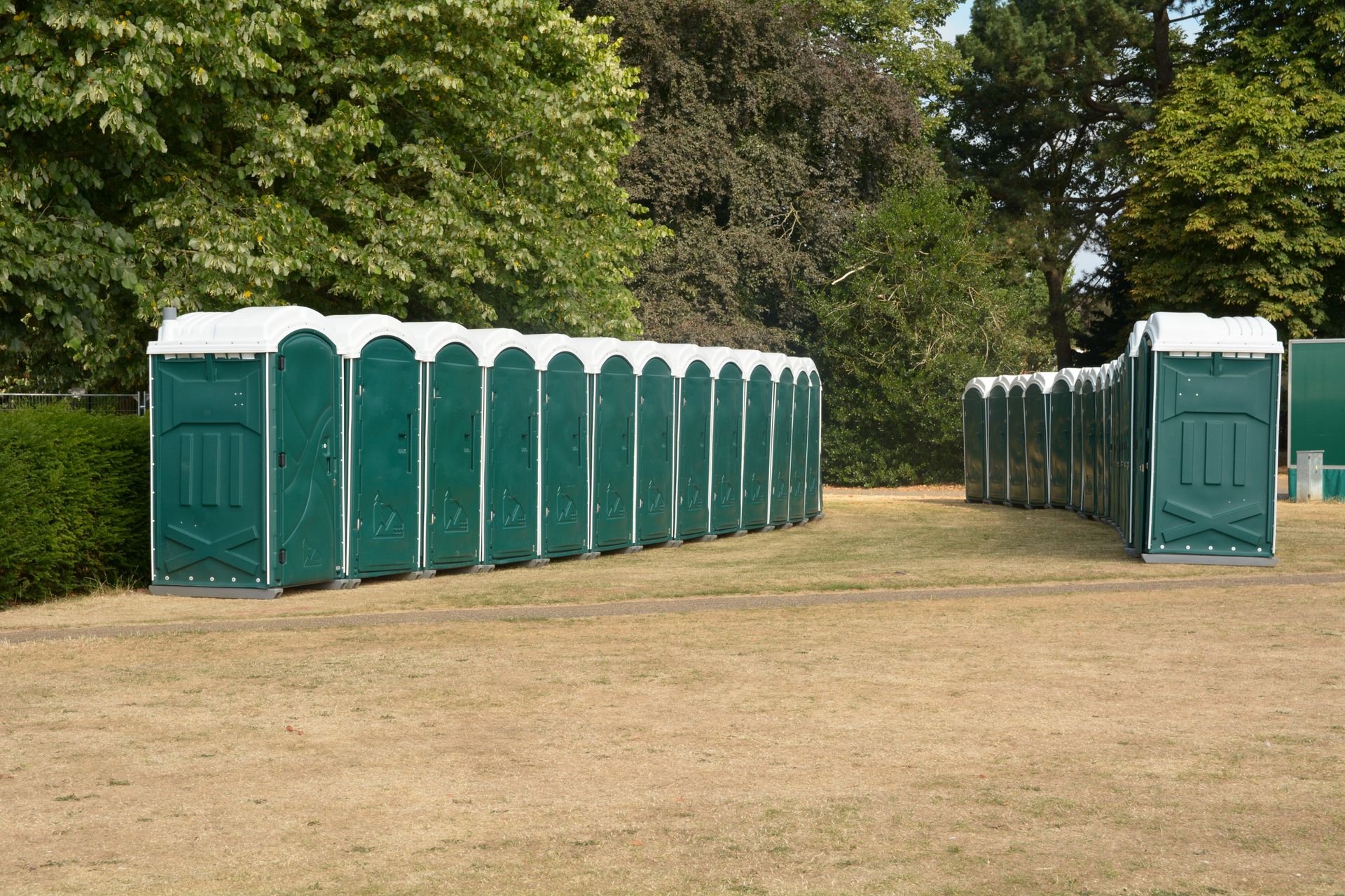 Rows of green portable toilets on a dry grassy field, trees in the background. Rows of green portable toilets on a dry grassy field, trees in the background.