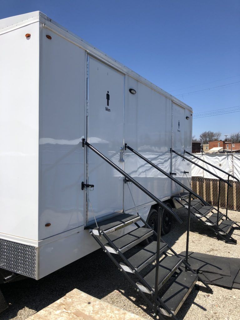 White portable restroom trailer with multiple entrances and steps.