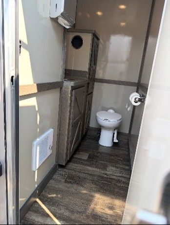 Interior of a portable restroom trailer with toilet, cabinet, and dispenser on wall.