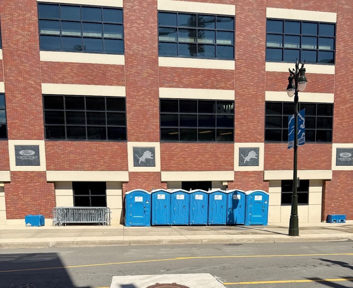 Five blue portable toilets on a gravel surface under a clear blue sky.