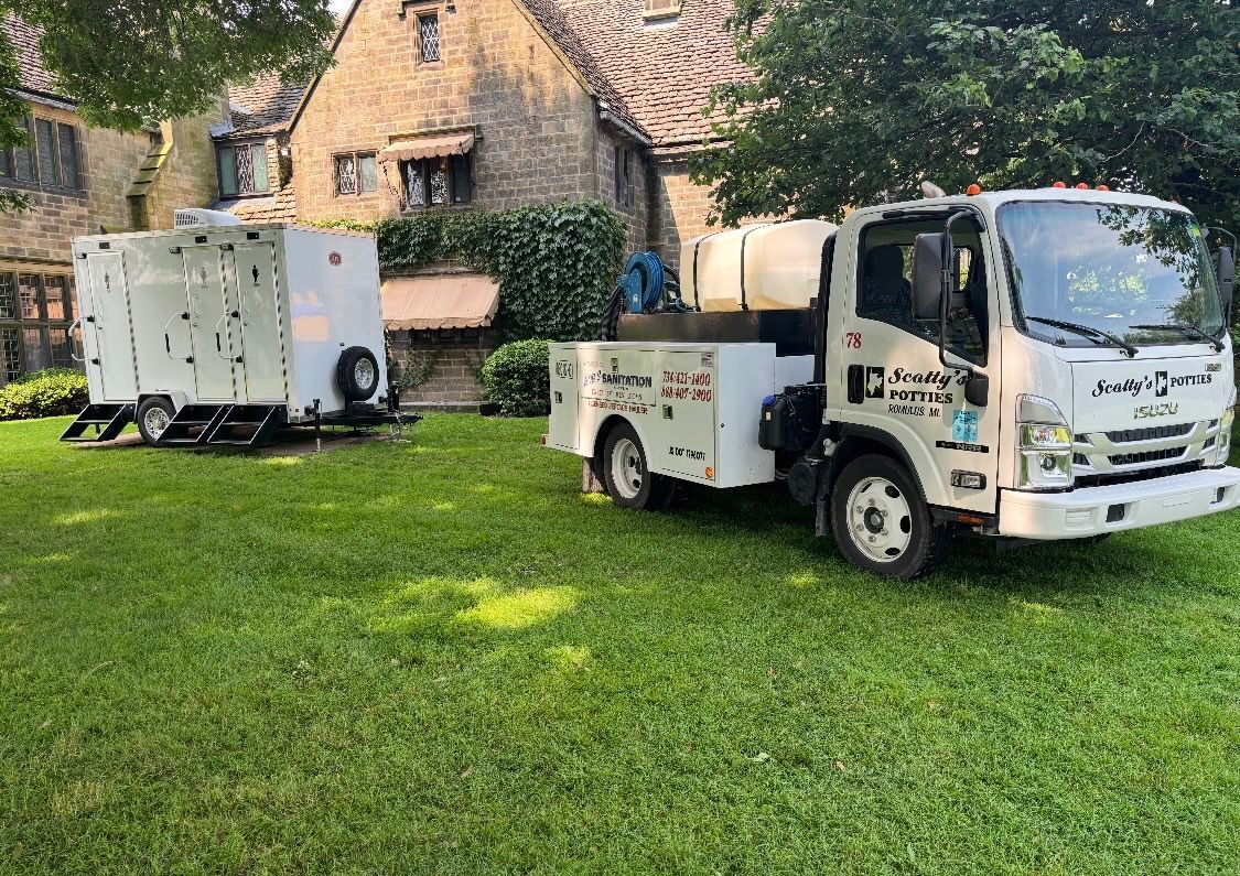 White utility truck and trailer on green lawn in front of a stone building.