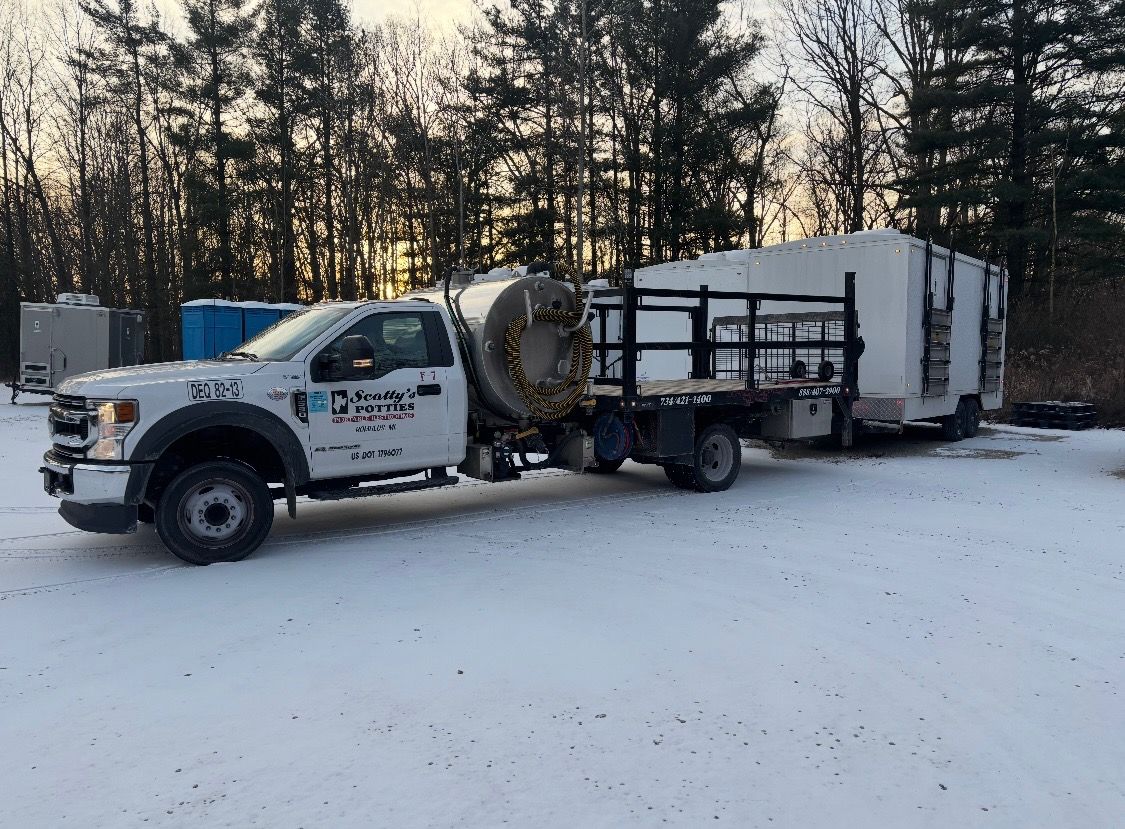White truck with a large tank and a rectangular structure on a flatbed, parked in a snowy area. Trees in the background.