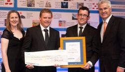 a group of people standing next to each other holding a framed check