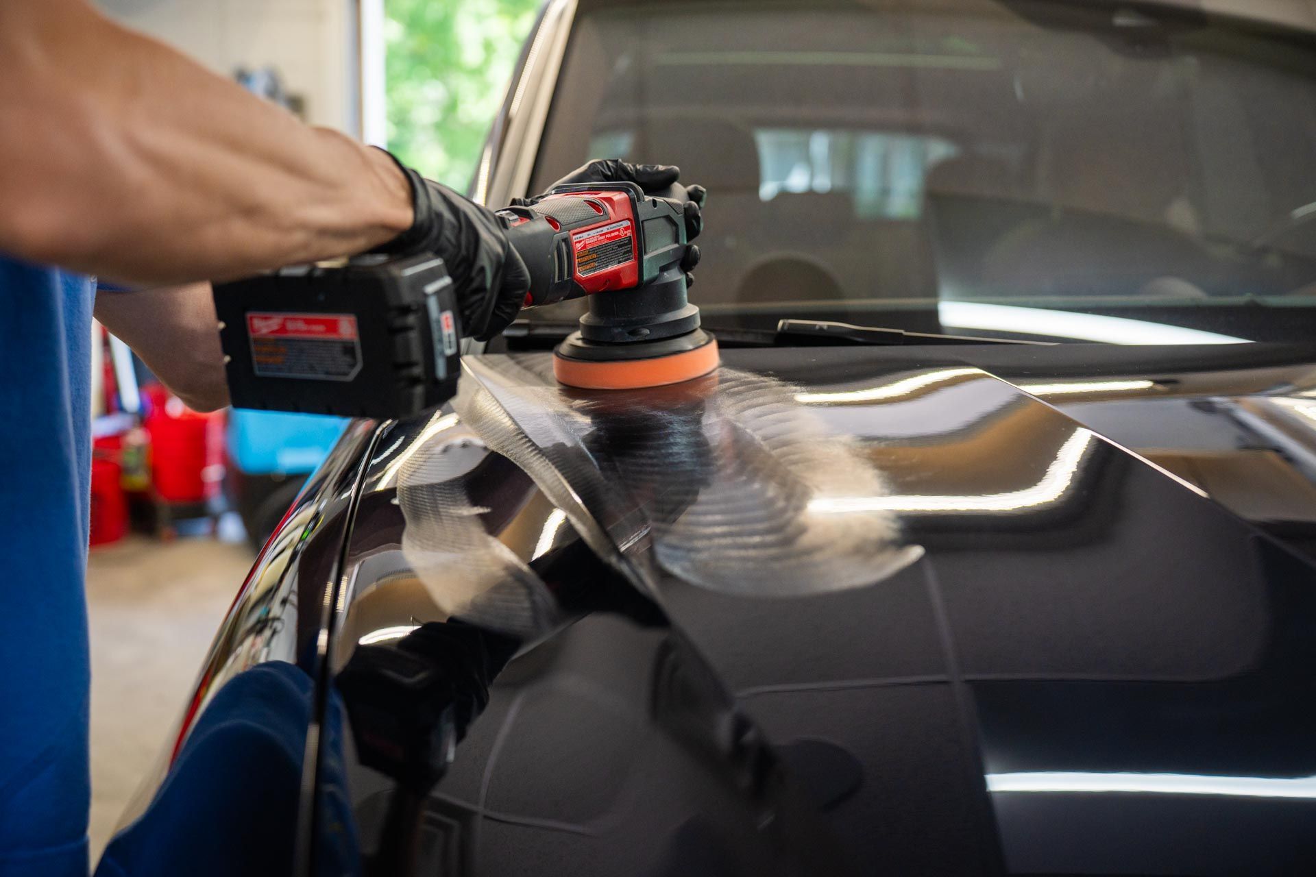 Buffer polishing a black car hood with a handheld power tool