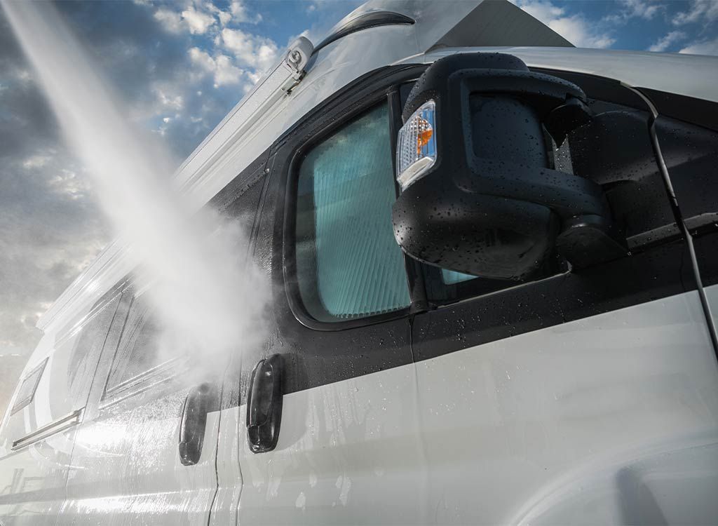 A white van being washed with a jet of water. Black side mirror and window visible.