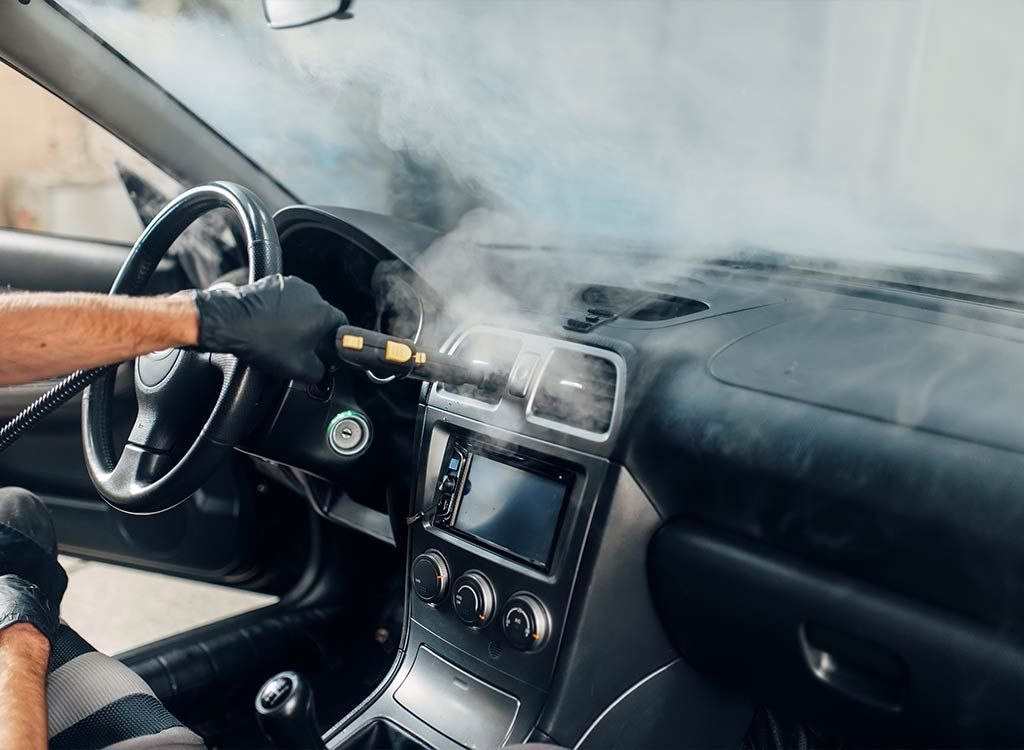 Black-gloved hand steaming a car dashboard. Steam fills the interior.