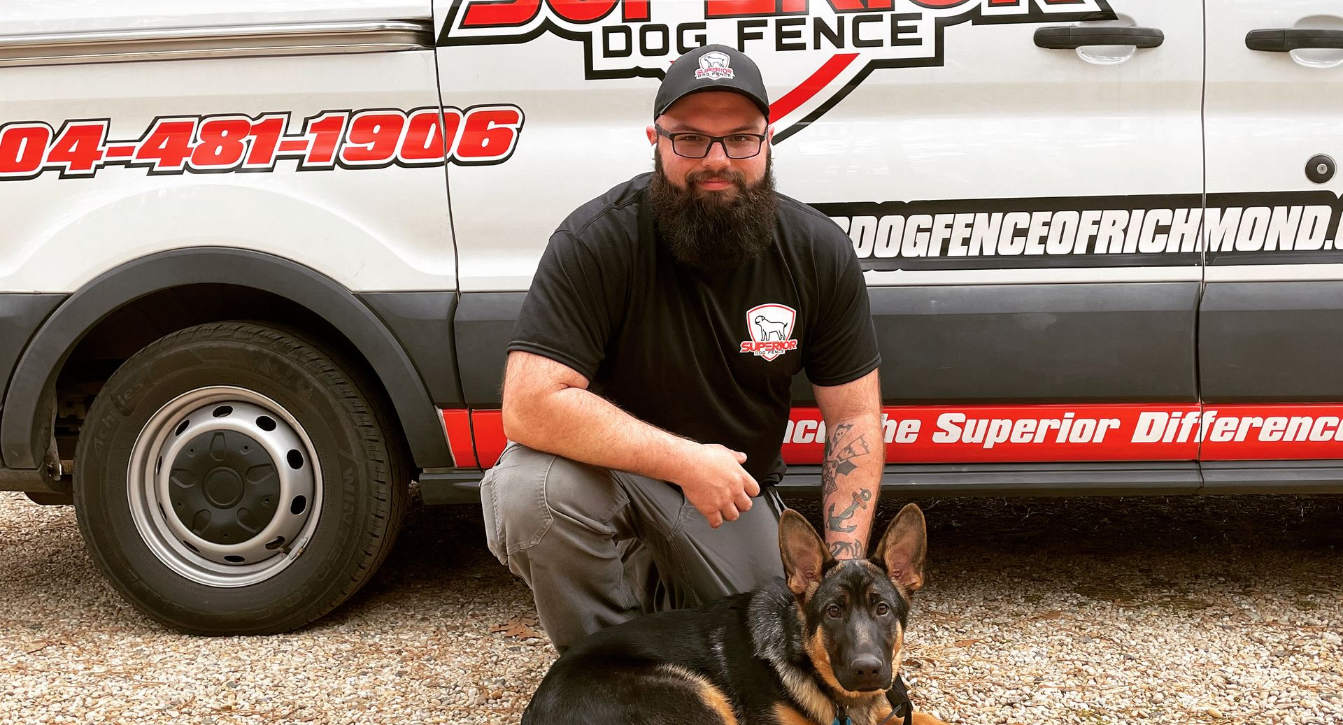 Man kneeling with German Shepherd dog in front of a branded van; black, red, and white colors.