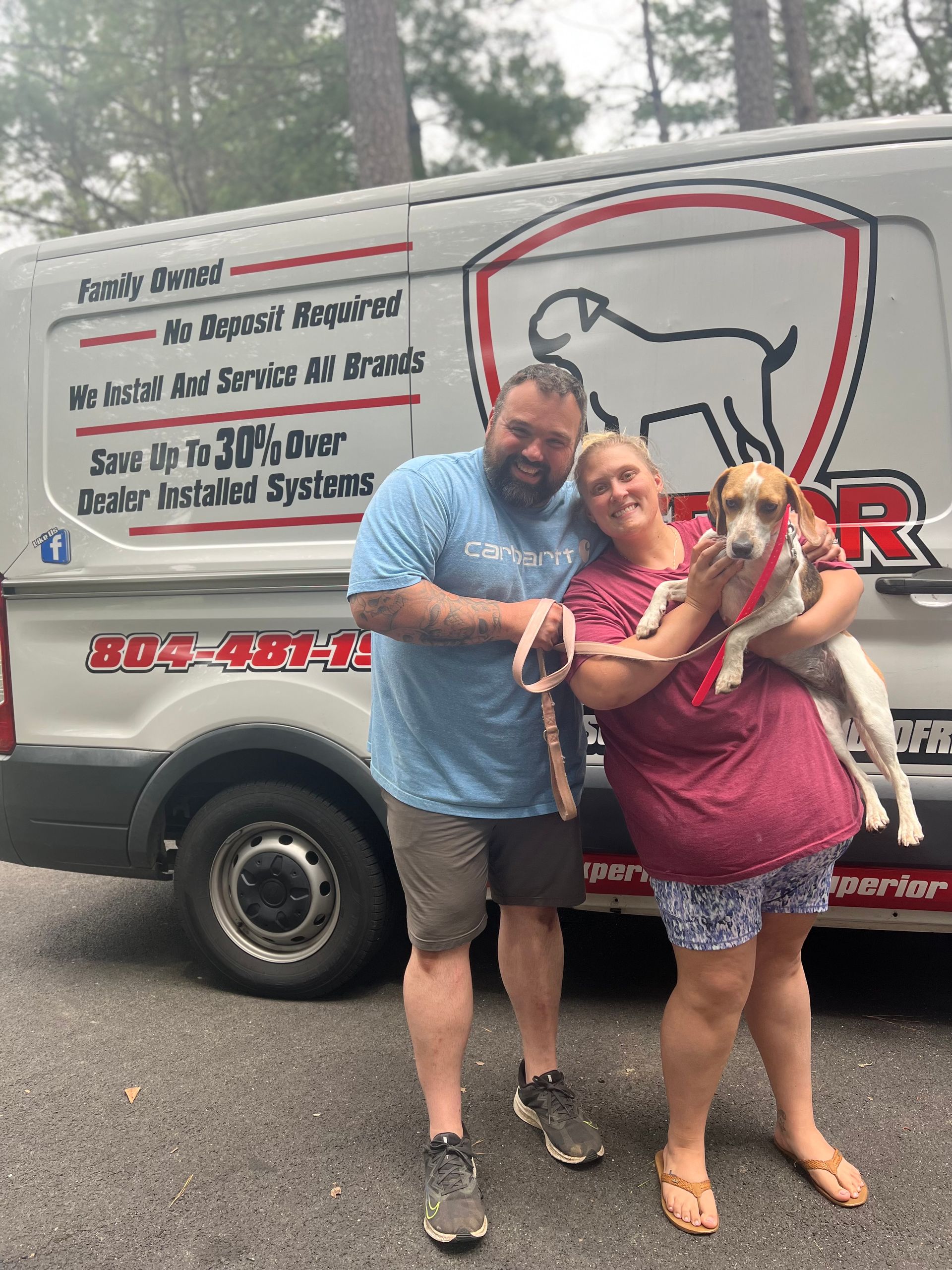 Couple and dog pose in front of a van. The van has a company logo and the text 