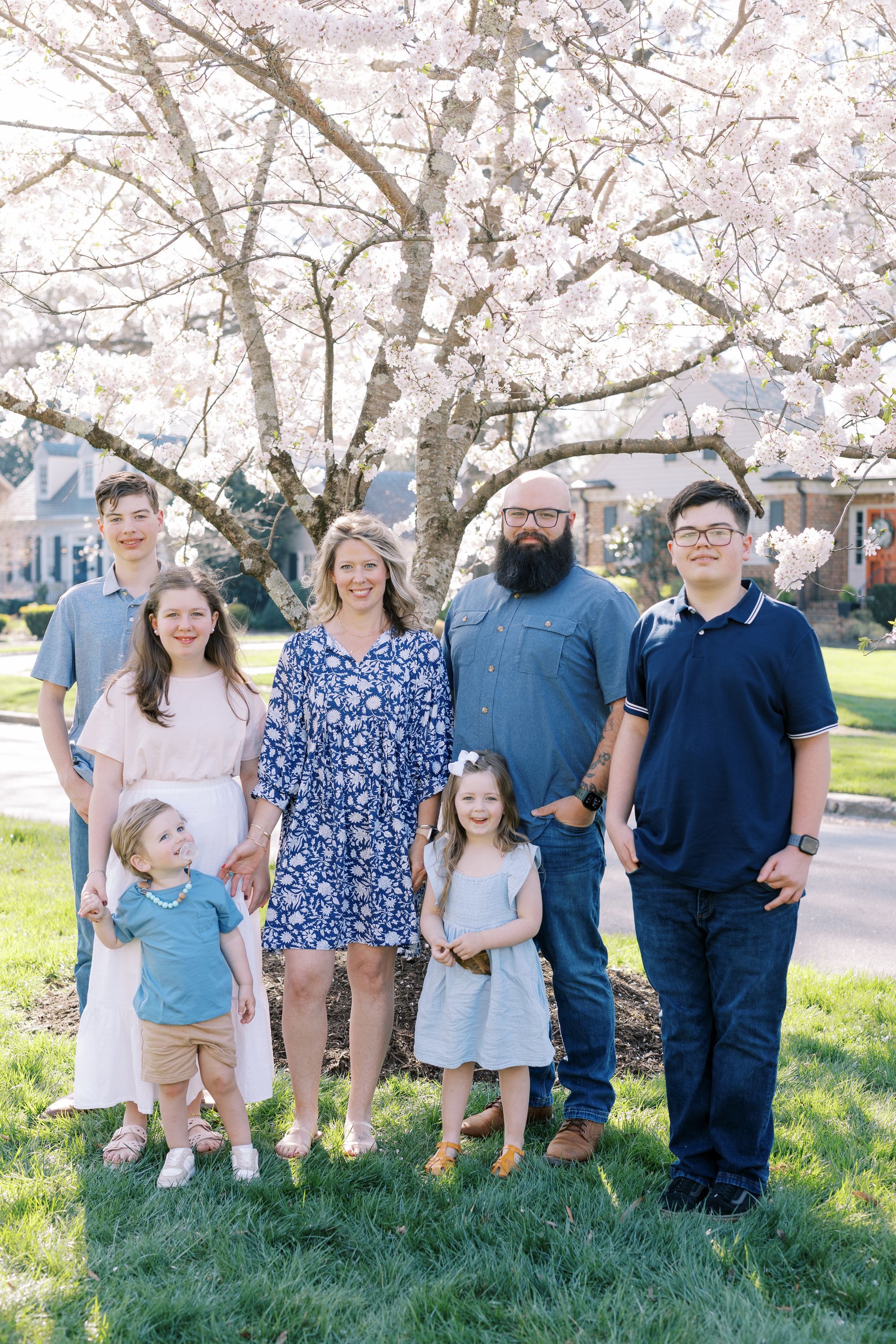 Family of six on stone steps; man with beard, woman holding baby, children smiling.
