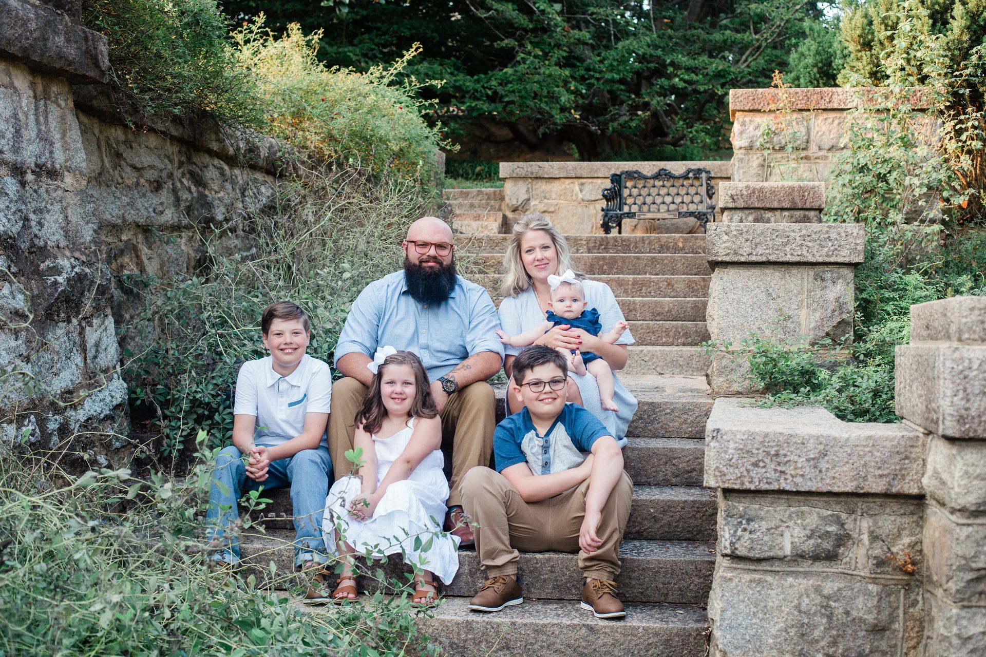 Family of six sits on stone steps in a park.