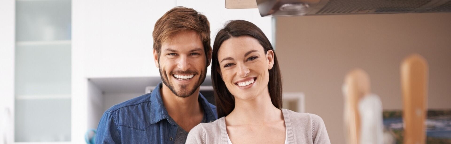A couple smiling while standing in a bright kitchen.