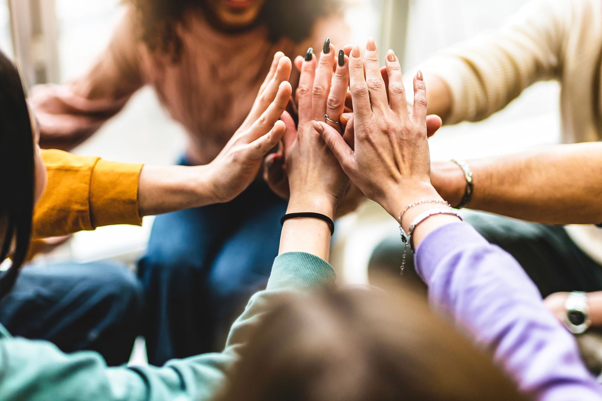 Hands stacked together in a group high-five, with colorful sleeves in a blurred indoor setting