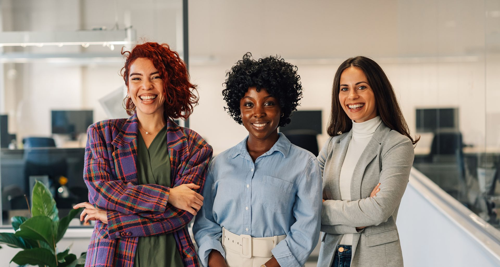 Three coworkers standing together in a modern office, smiling with arms crossed