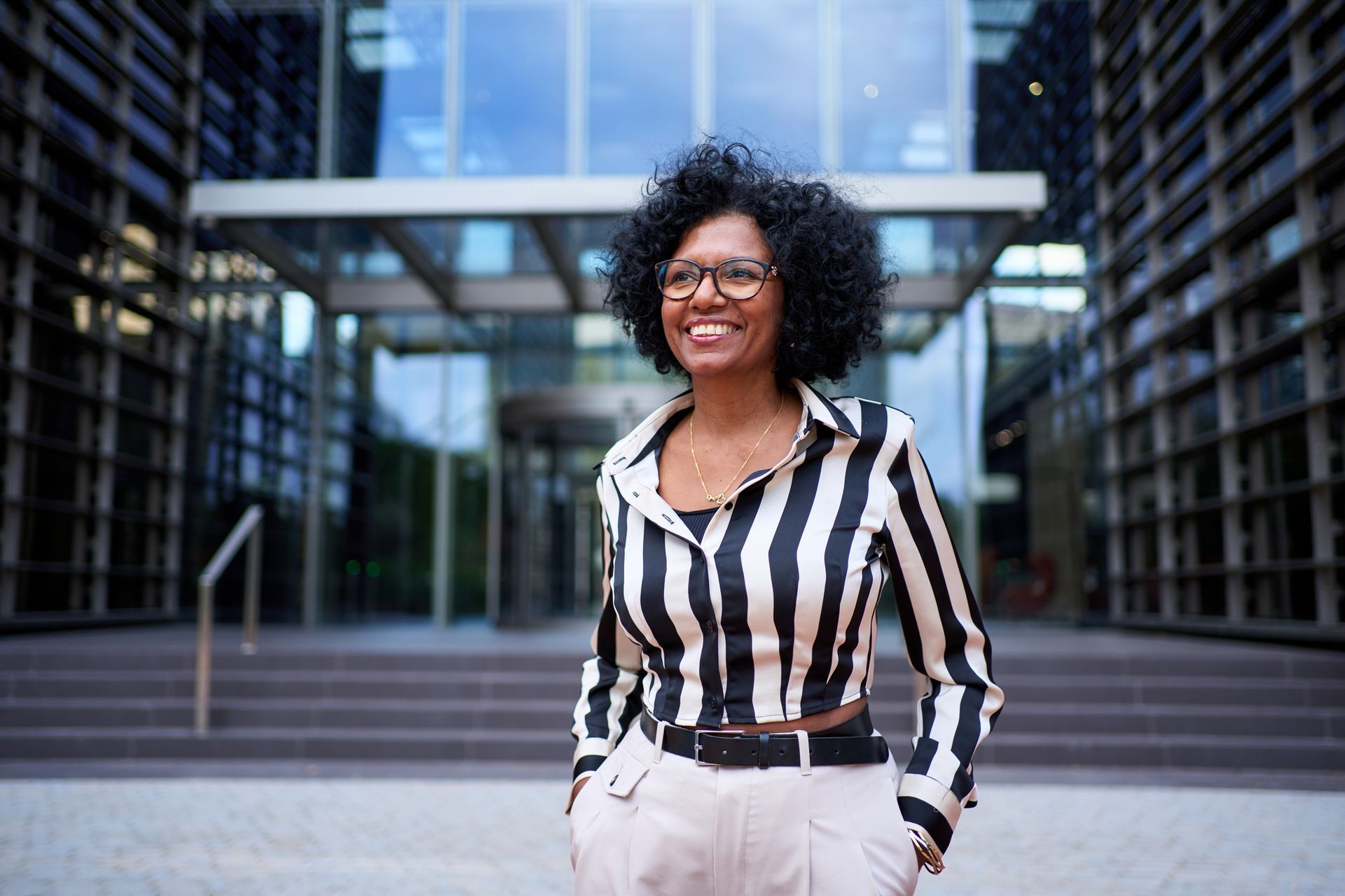 Woman standing outside a modern office building, wearing a black-and-white striped blouse and smiling.