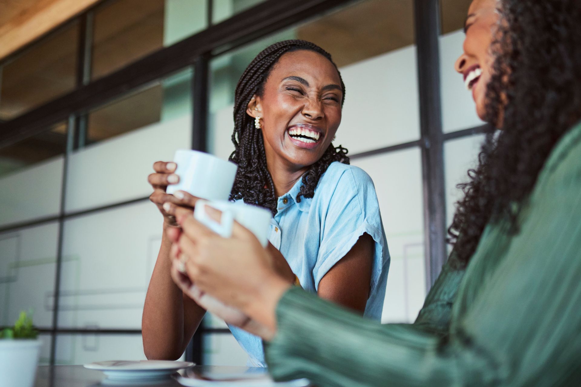 Two coworkers smiling and talking over coffee at a table indoors