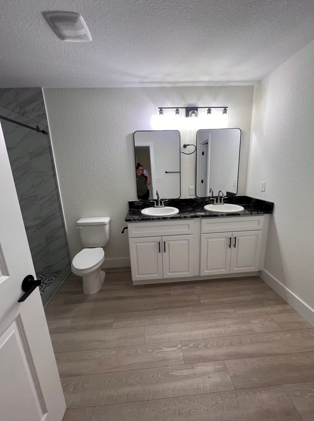 Modern bathroom with double vanity, mirrors, toilet, and walk-in shower, in gray and white tones
