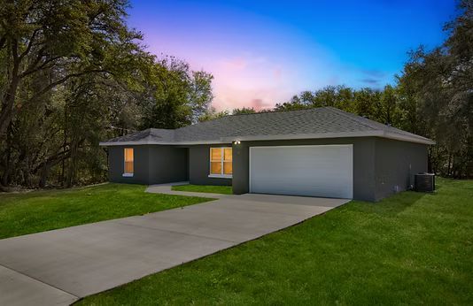 Single-story gray house at dusk with lit windows, a two-car garage, and a curved concrete driveway.