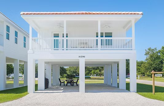 Stilted white beach house with a covered porch and open ground level under a bright blue sky