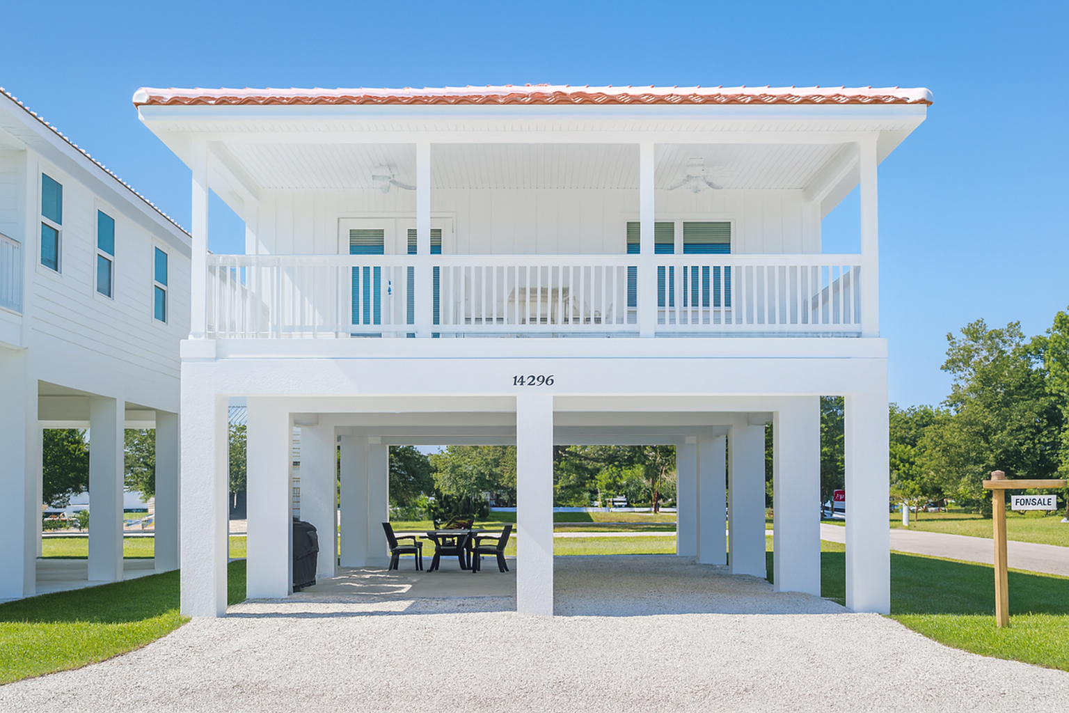 White raised beach house with wraparound porch and open parking below on a sunny day