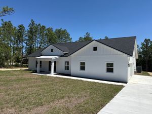 White single-story house with dark roof and covered porch beside a concrete driveway under a blue sky