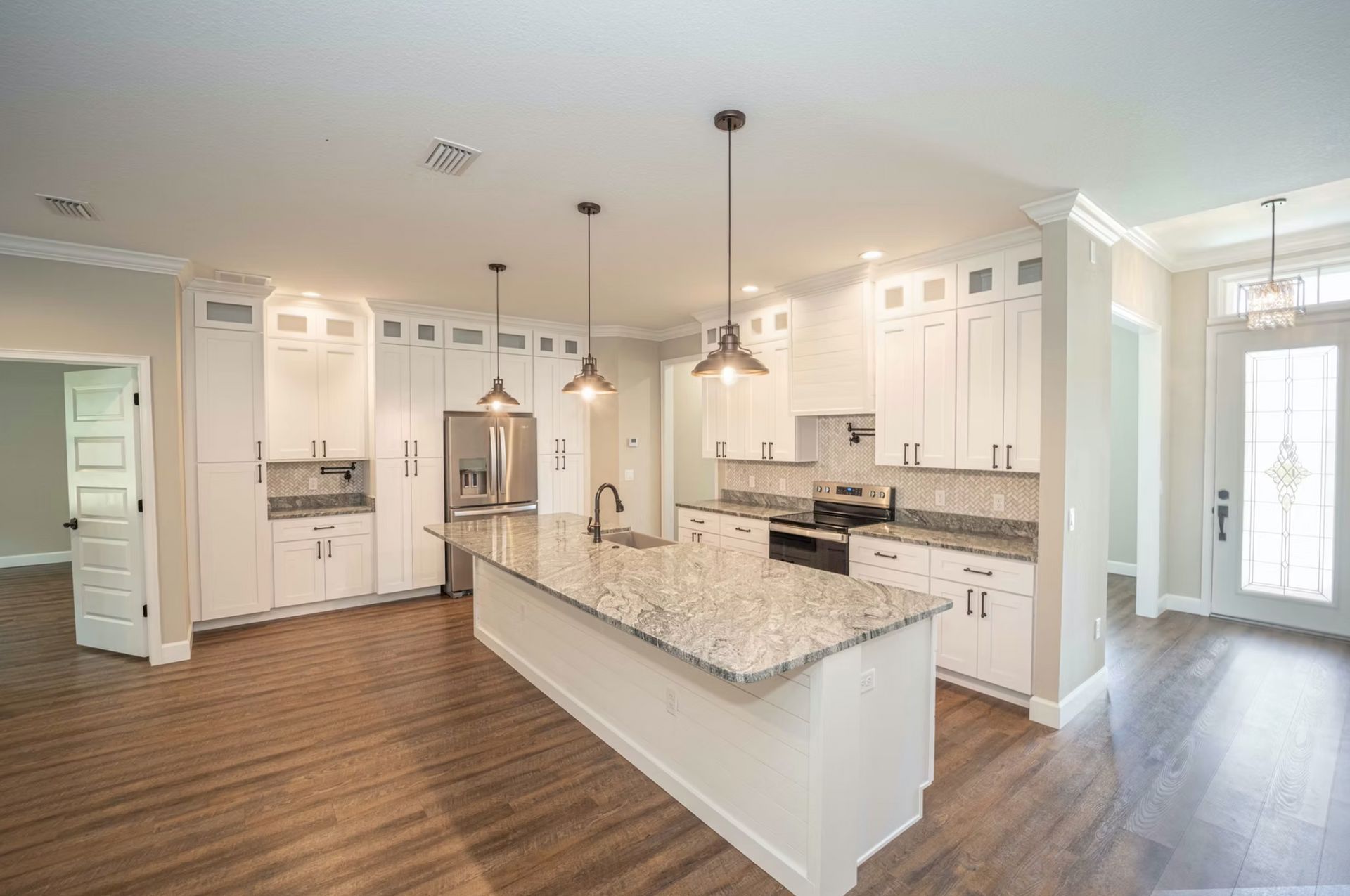 Bright modern kitchen with white cabinets, granite island, pendant lights, and wood flooring