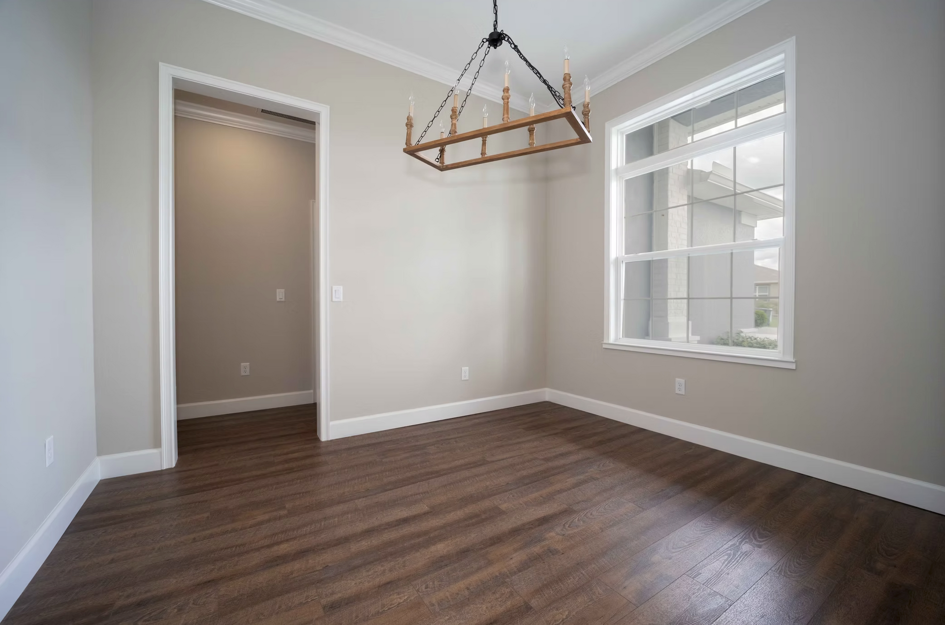 Empty beige dining room with dark wood floors, a window, and a modern hanging light fixture