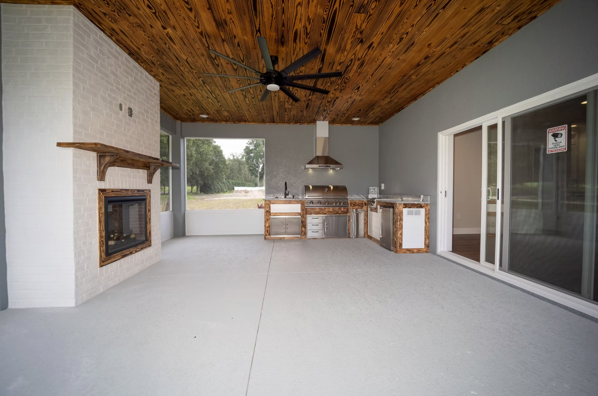 Covered patio with wood ceiling, fireplace, dining table, and sliding glass doors.
