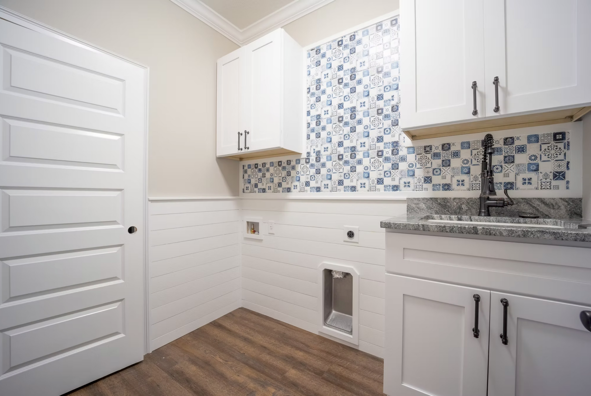Bright laundry room with white cabinets, blue tile backsplash, and wood-look floor.