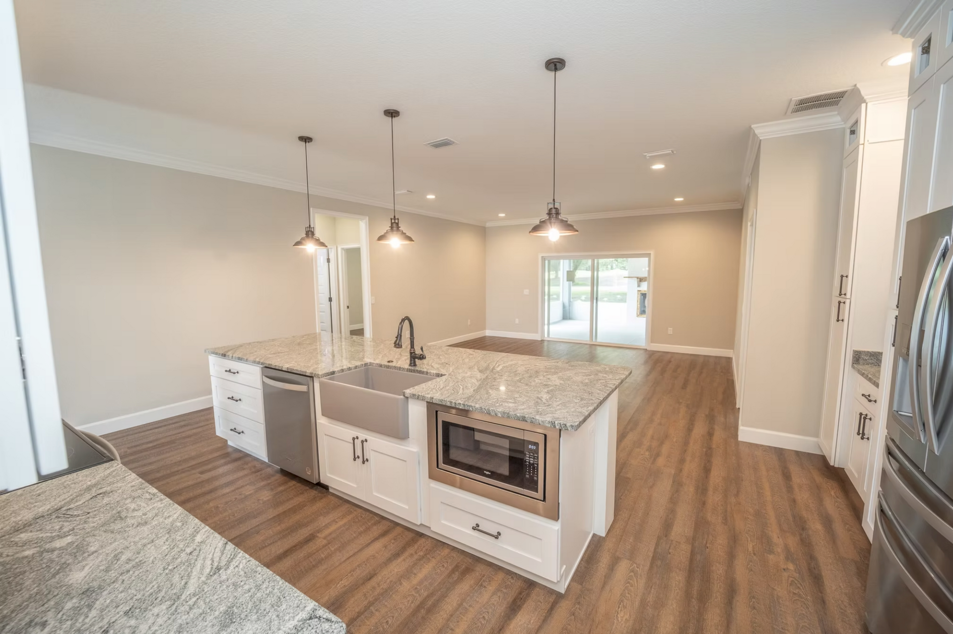 Bright kitchen with white island, granite counters, pendant lights, and wood-look flooring in an open layout