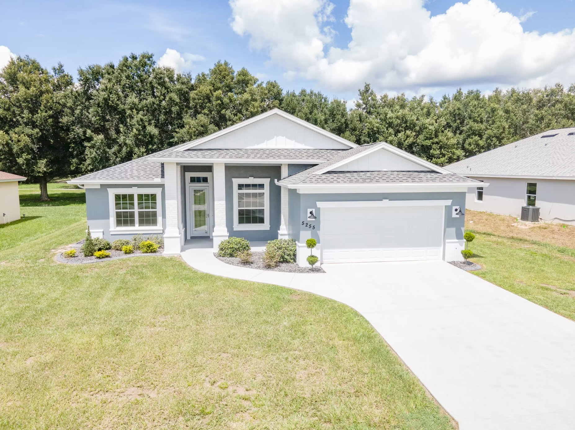 Gray single-story house with white trim, two-car garage, and a green front lawn on a sunny day