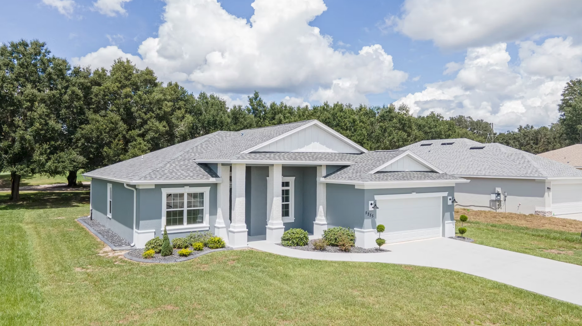 Single-story gray house with white trim, front porch, garage, and a well-kept lawn under a sunny sky