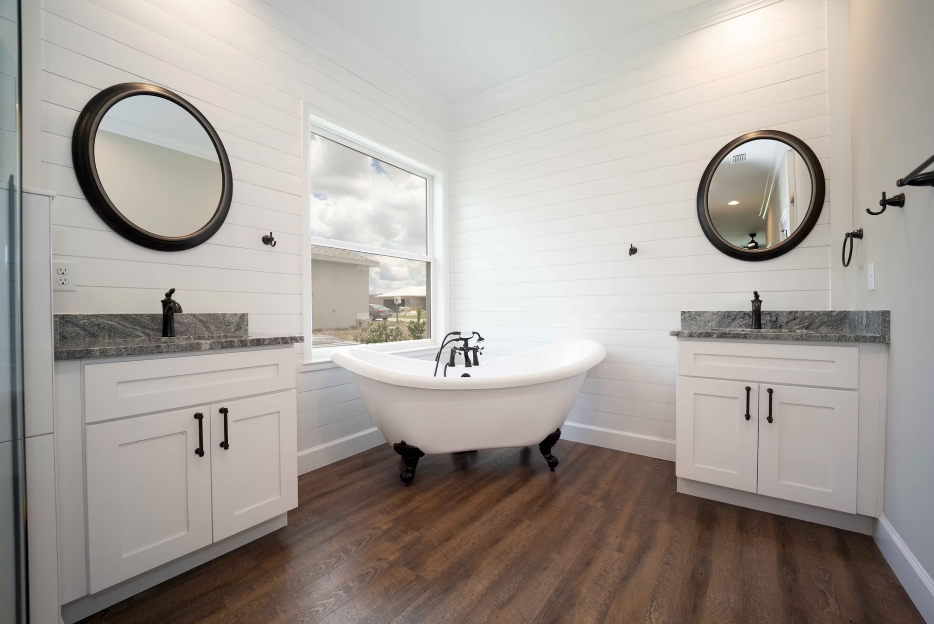 Modern bathroom with freestanding tub, two round mirrors, and white vanities on wood floors