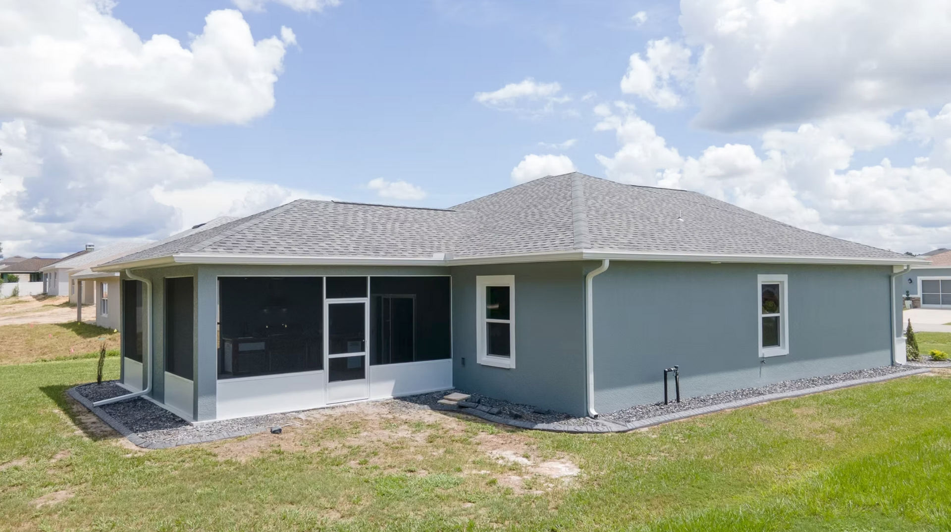 Single-story gray house with screened porch and grassy yard under a cloudy sky