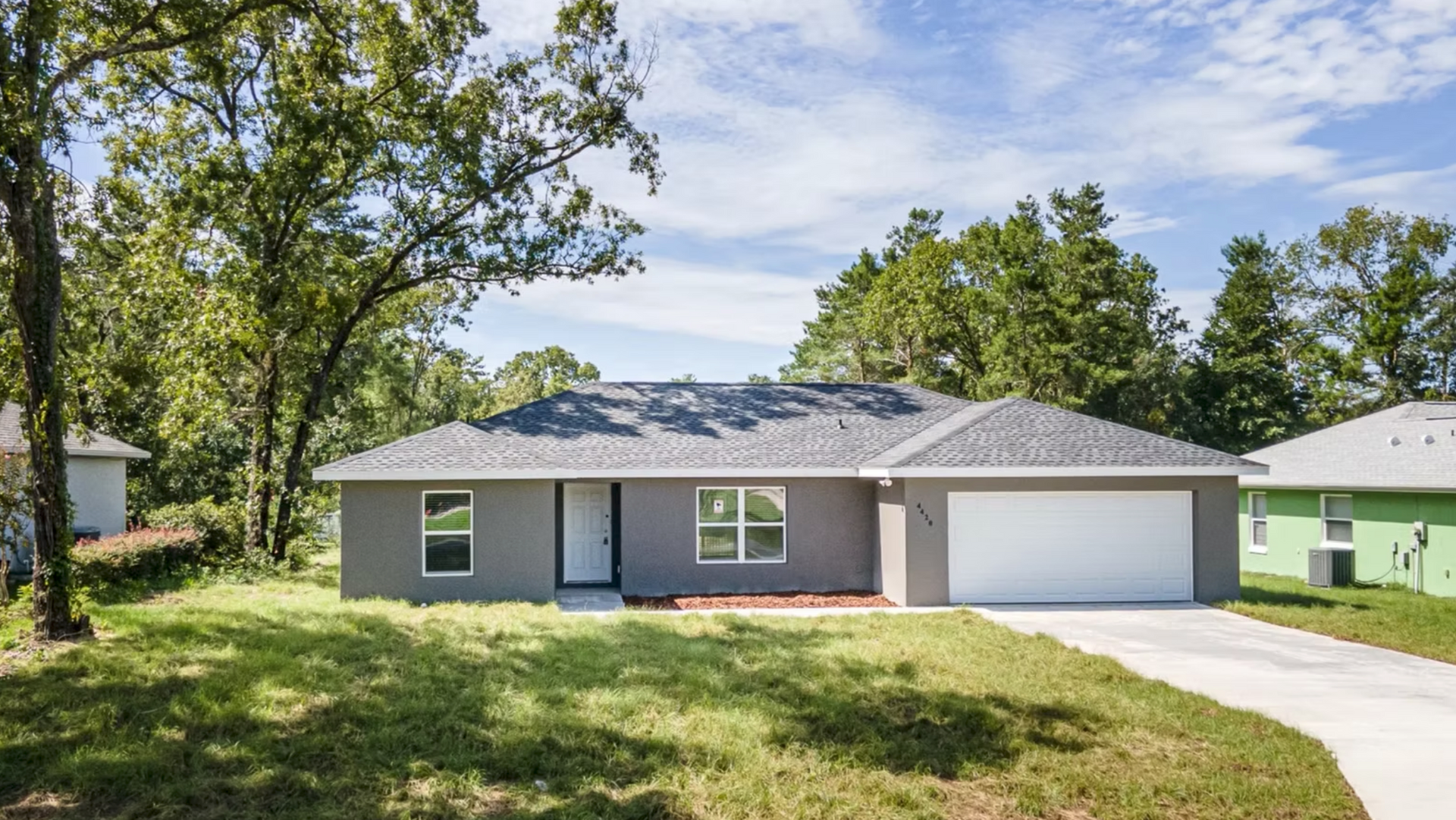 Single-story gray house with white garage, blue front door, and trees in the yard