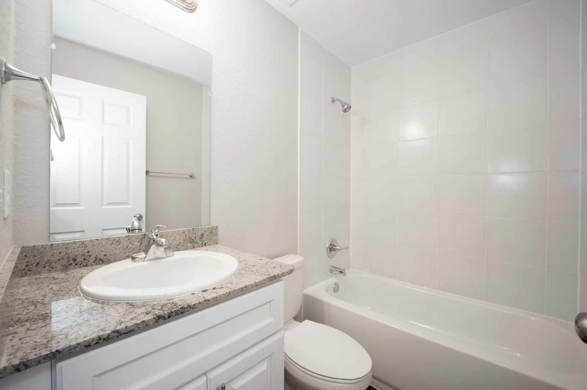 Bright bathroom with granite vanity, mirror, sink, toilet, and white bathtub/shower tiles