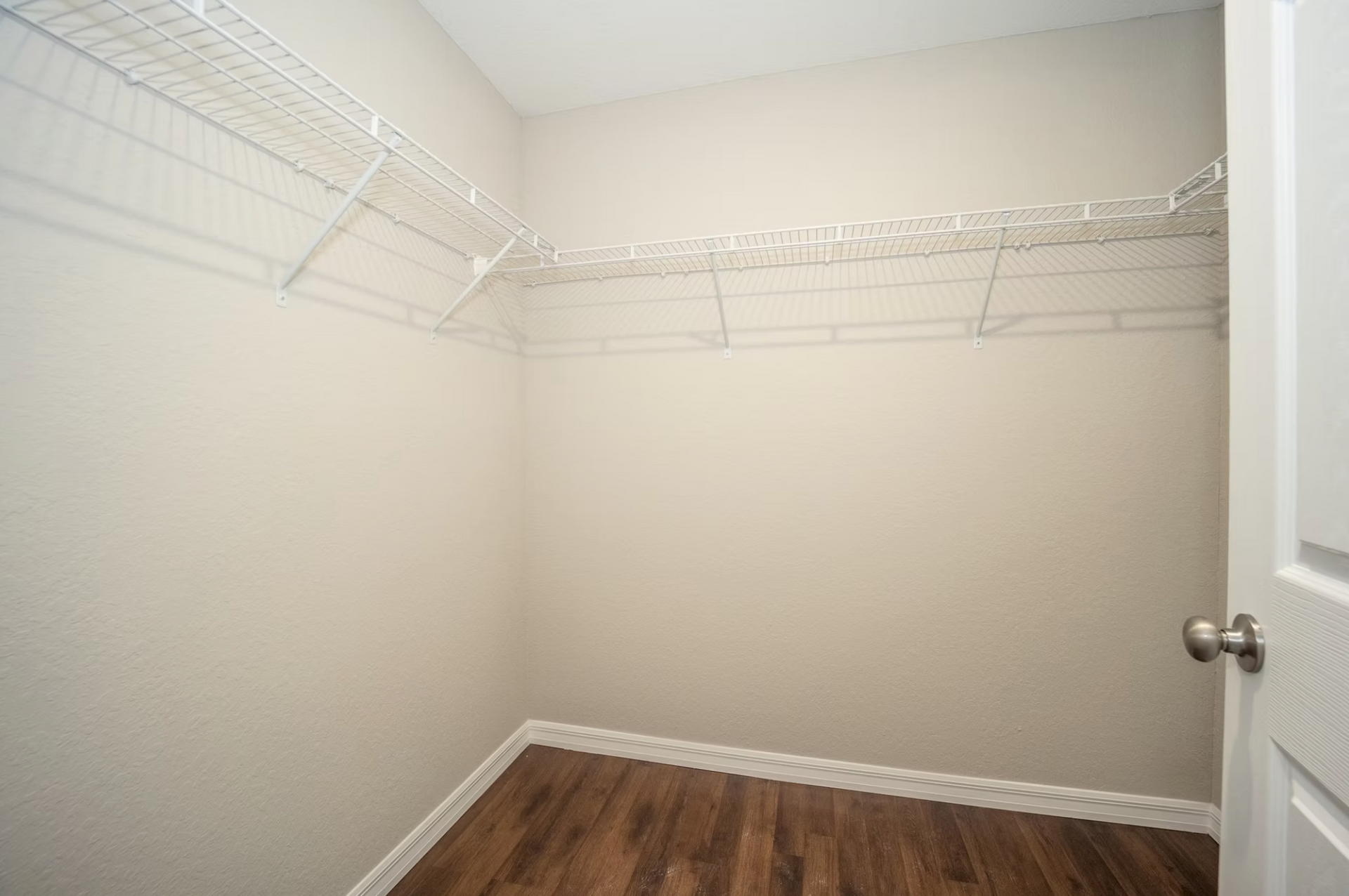 Empty beige walk-in closet with wire shelving and wood-look floor.