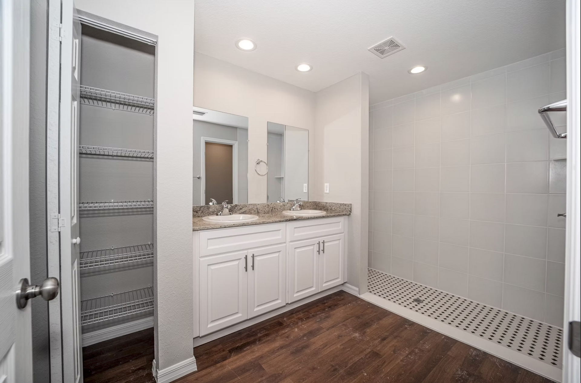 Modern bathroom with double vanity, large mirror, tiled shower, and open shelving closet on the left.
