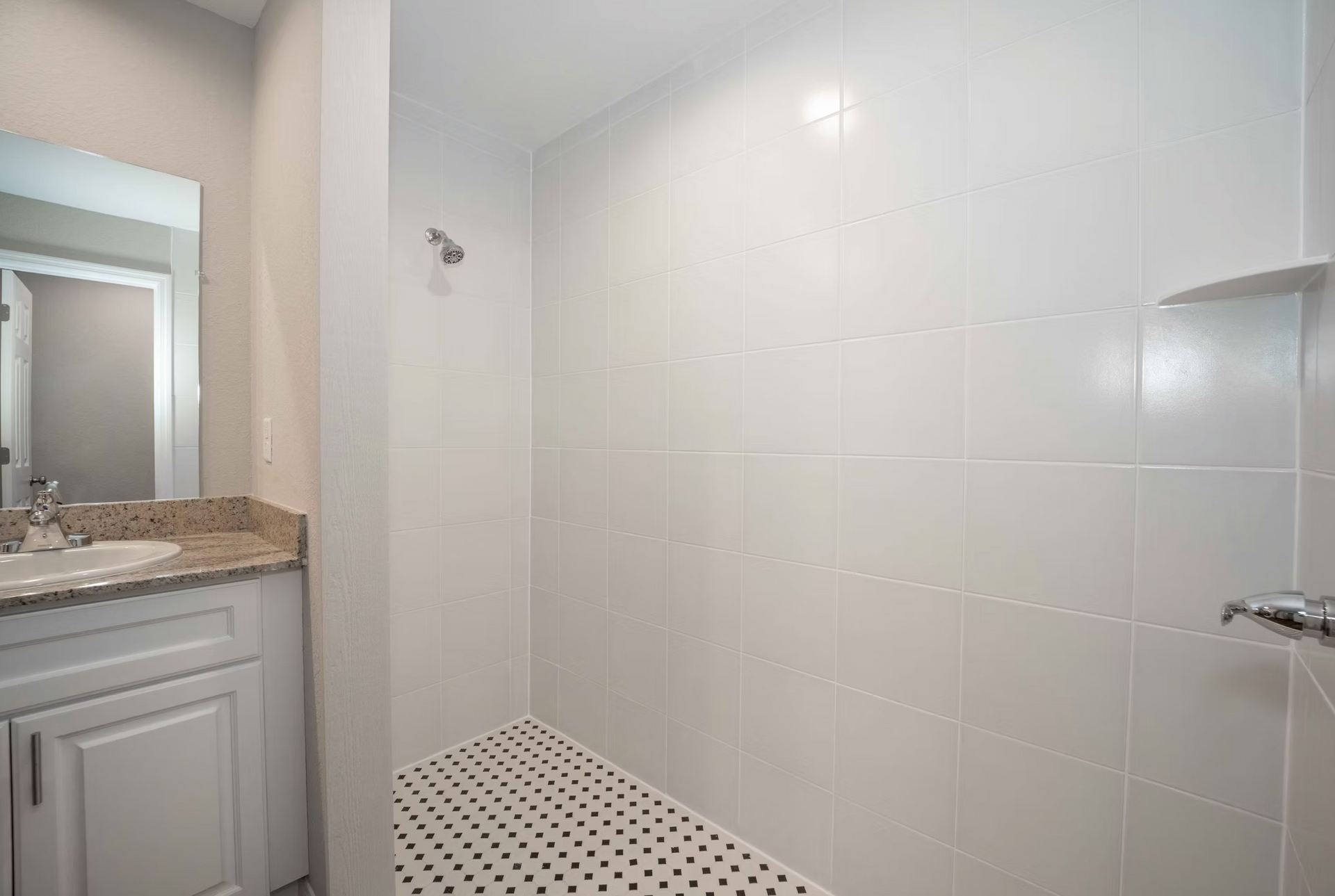 Bright white tiled walk-in shower with pebble floor beside a vanity and mirror