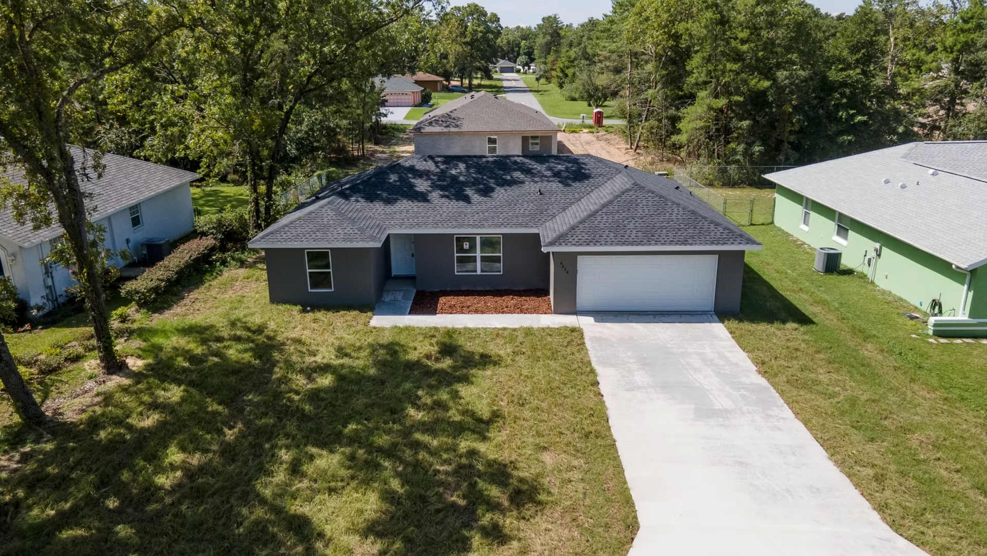 Aerial view of a single-story gray house with a white driveway and green lawn