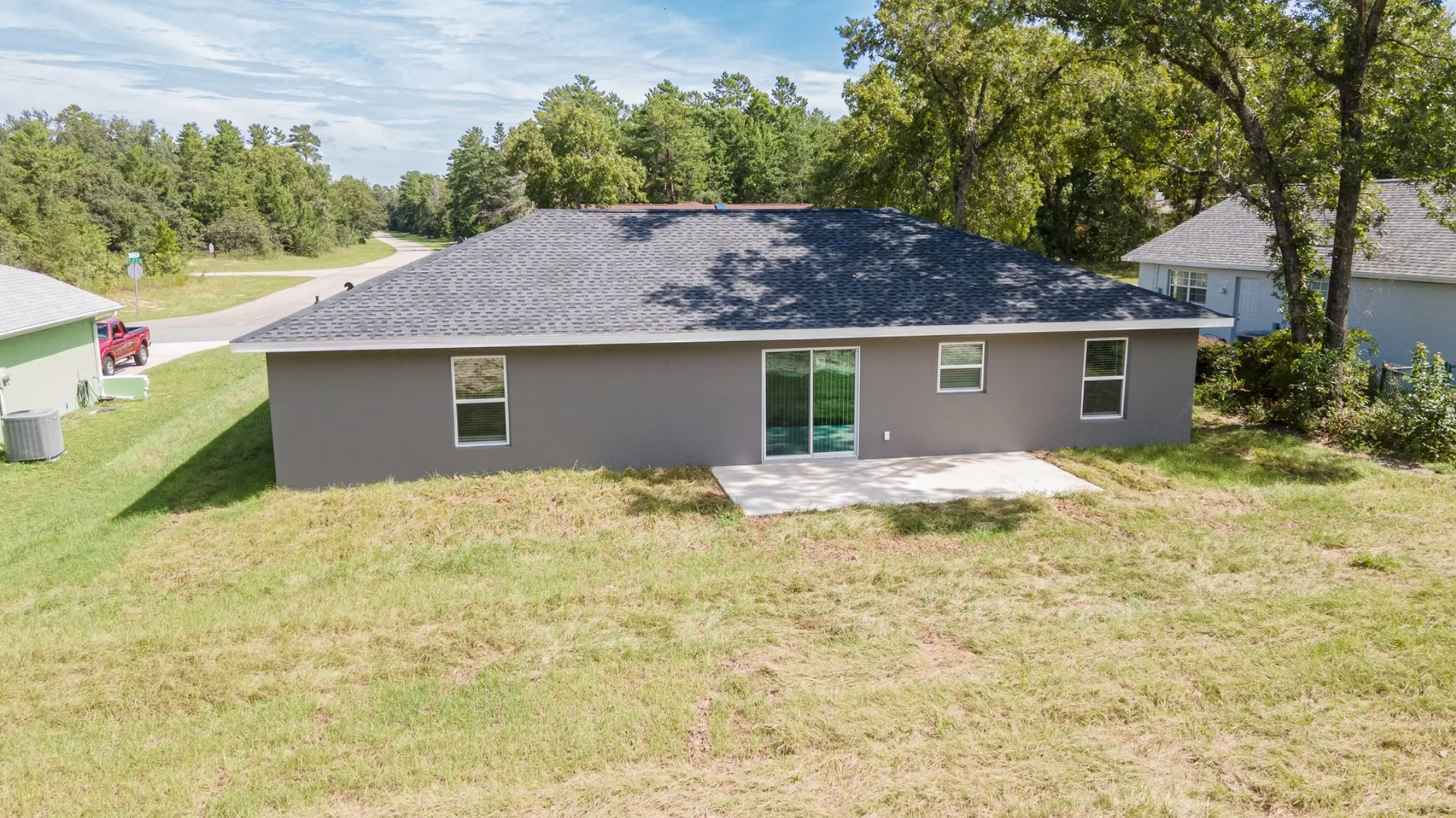 Single-story gray house with dark roof, small front patio, and large grassy yard under trees.