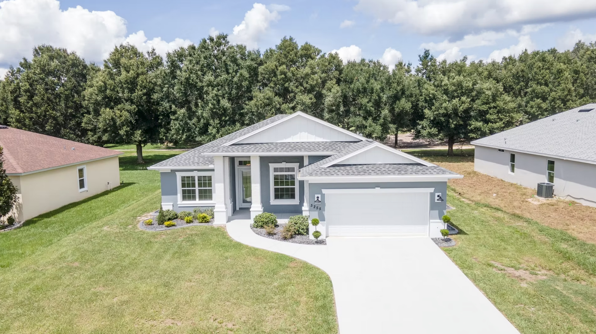 Gray single-story house with a white garage, curved driveway, and green lawn