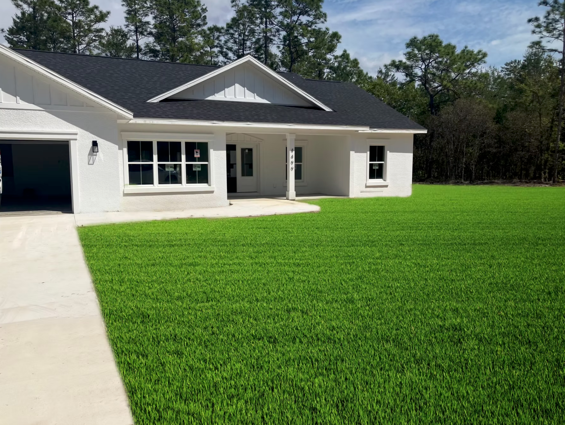 White house with a dark roof and large green lawn under a blue sky