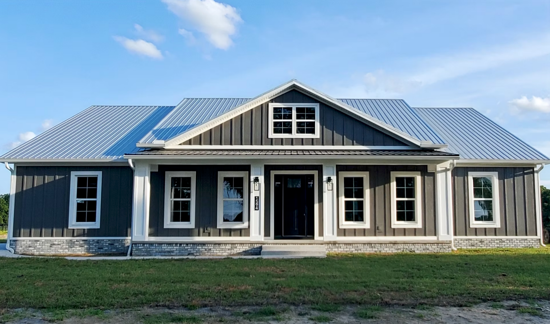 Front view of a gray farmhouse-style house with a metal roof and front porch under a blue sky
