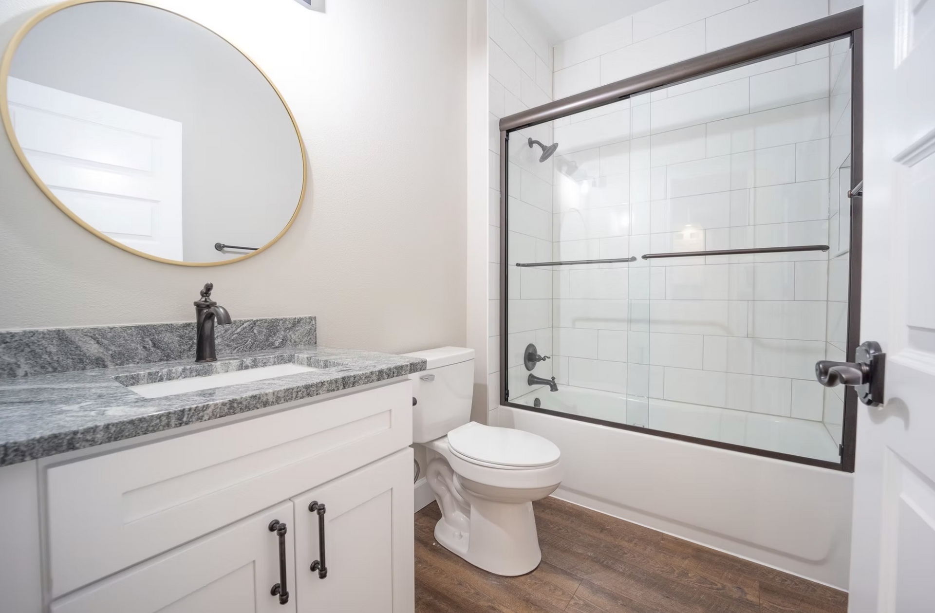 Modern bathroom with white vanity, round mirror, toilet, and glass-enclosed shower.