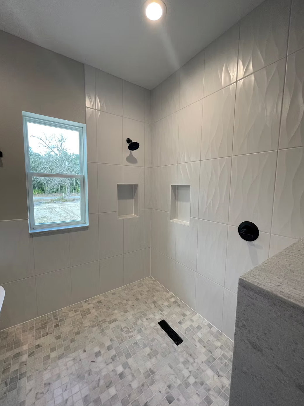 Tiled shower with window, wall niches, and black shower controls in a bright bathroom.
