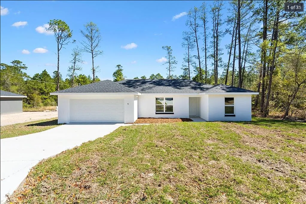 Single-story white house with a two-car garage and grassy front yard under a clear blue sky
